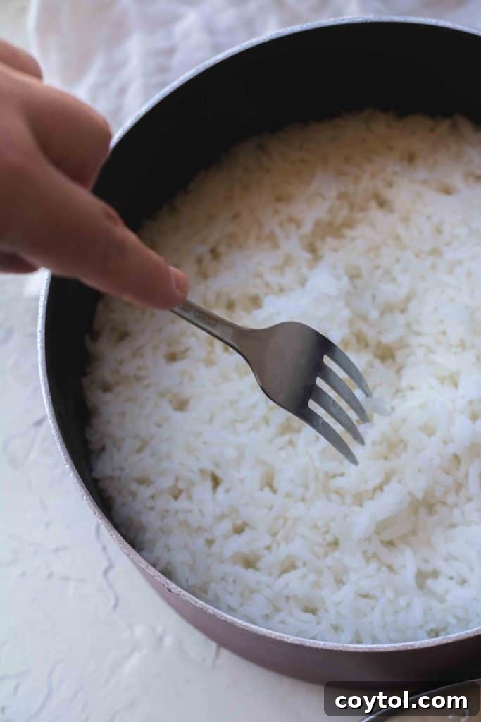 Fluffing white rice with a fork after resting