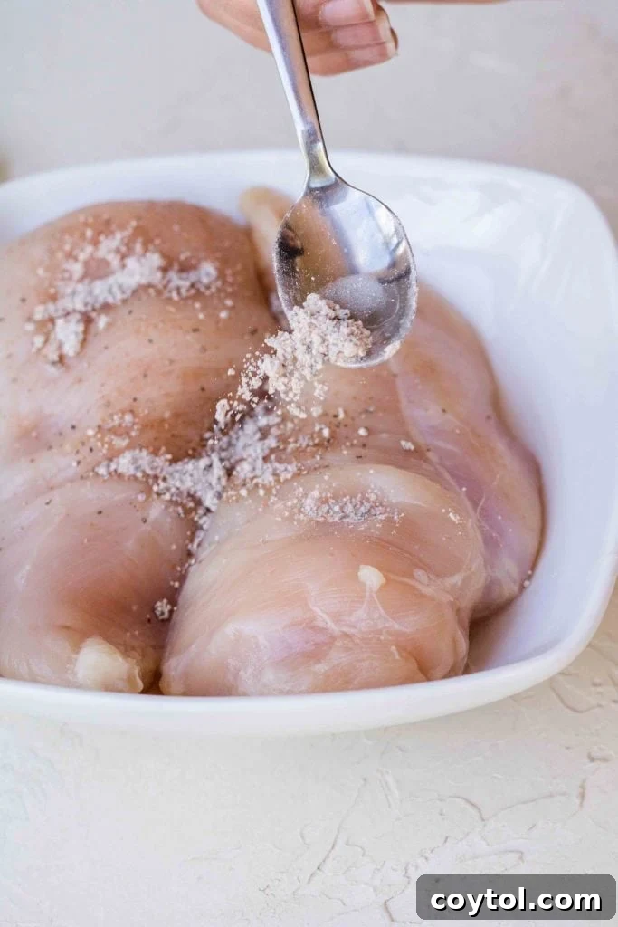 Seasoning chicken breast with a mix of black pepper, chili powder, and garlic powder.
