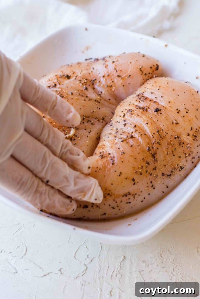 Drizzling olive oil over the seasoned chicken breasts in a bowl.