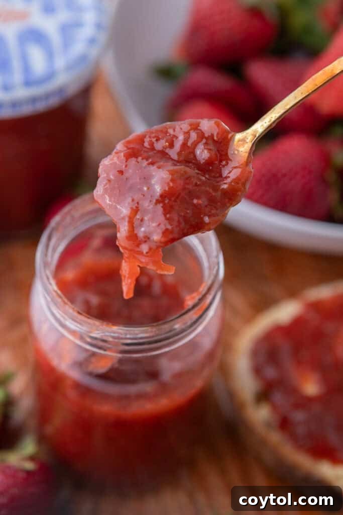 Homemade Strawberry Rhubarb Jam Without Pectin 2 A jar of homemade strawberry rhubarb jam with a spoon, highlighting its rich color and texture.