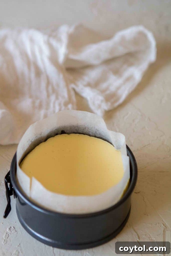 Baked 4-inch cheesecake cooling in springform pan lined with parchment paper