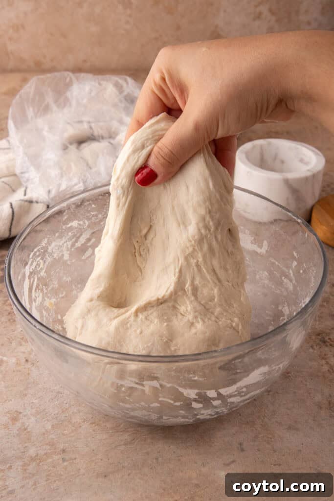 Hands performing the first stretch and fold on sourdough dough in a bowl.
