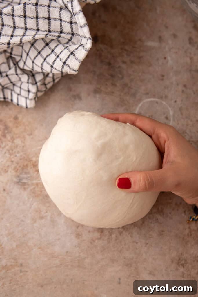 Hands performing final shaping on sourdough dough, tucking edges underneath.