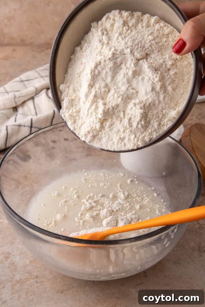 Close-up of bread flour, water, and active sourdough starter being mixed in a large bowl.