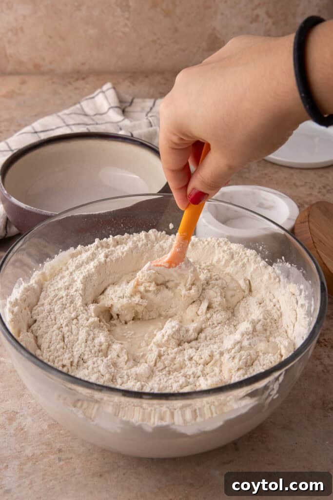 Hands gently mixing the shaggy sourdough dough in a bowl, showing hydration.