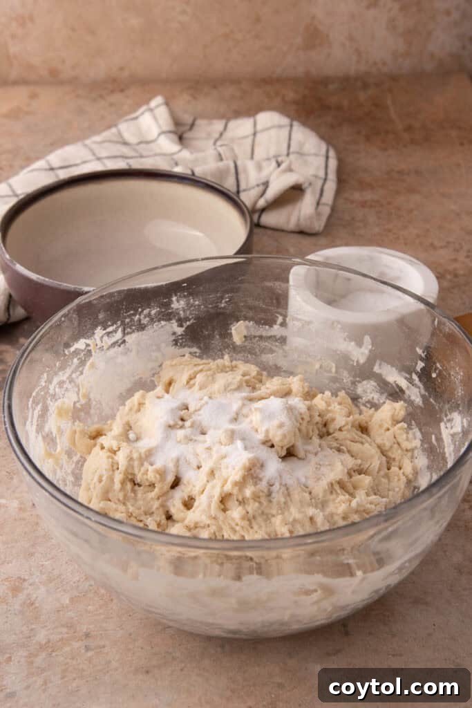 Salt being sprinkled over the dough in a bowl.