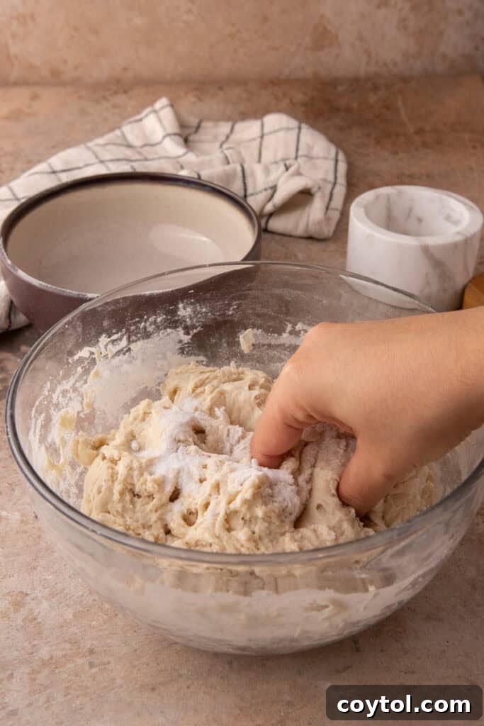 Hands gently mixing salt into the sourdough dough in a bowl.