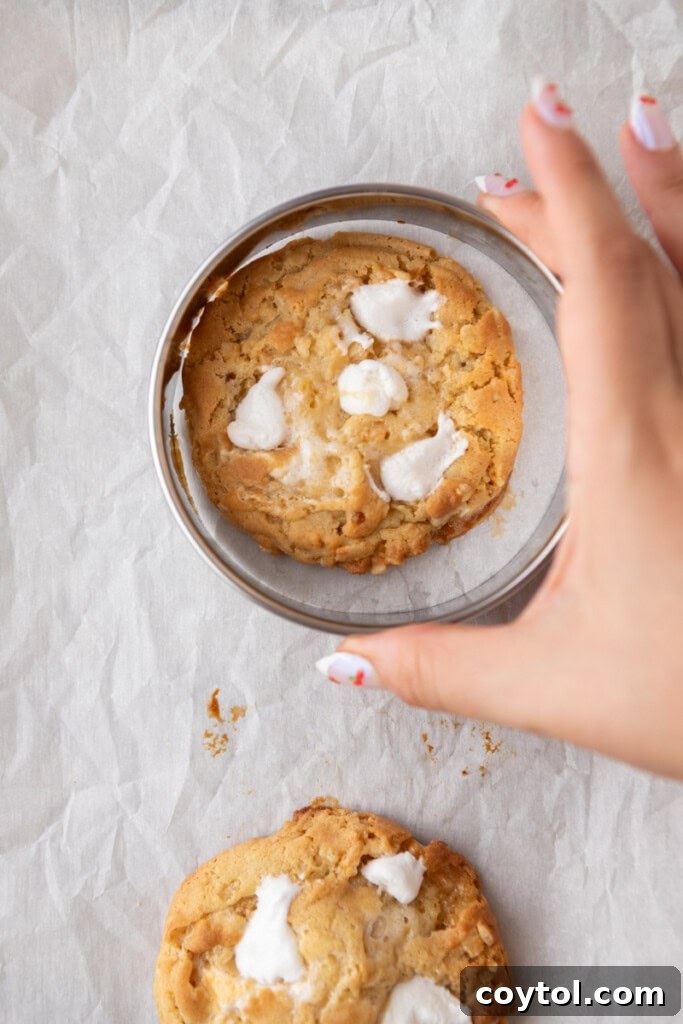 A hand gently swirling a warm cookie inside a larger cookie cutter to create a perfect circular shape.