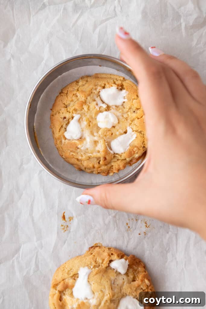 A hand applying half mini marshmallows onto a hot, freshly baked cookie to create the signature look.