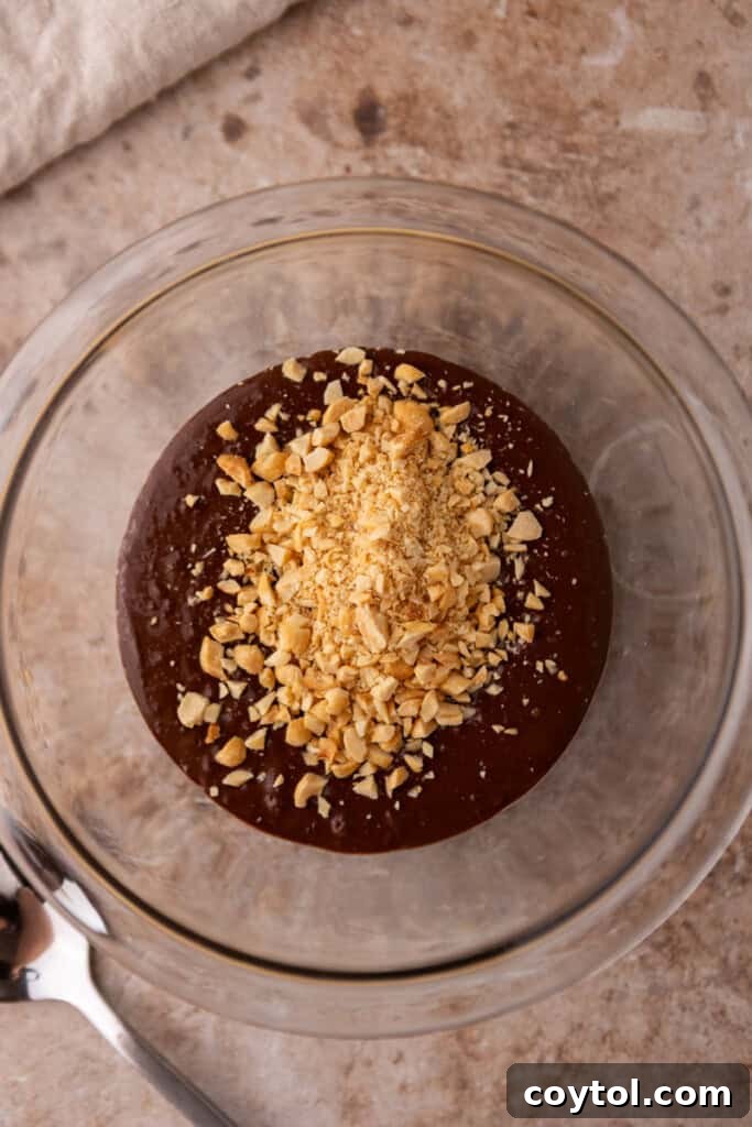 Ultimate Stroopwafel Choco Tacos Caramel Chocolate Perfection 9 Melted chocolate being stirred with chopped peanuts in a small bowl.