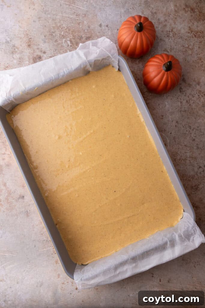 The creamy pumpkin cheesecake filling being poured evenly over the croissant dough base in the baking pan.