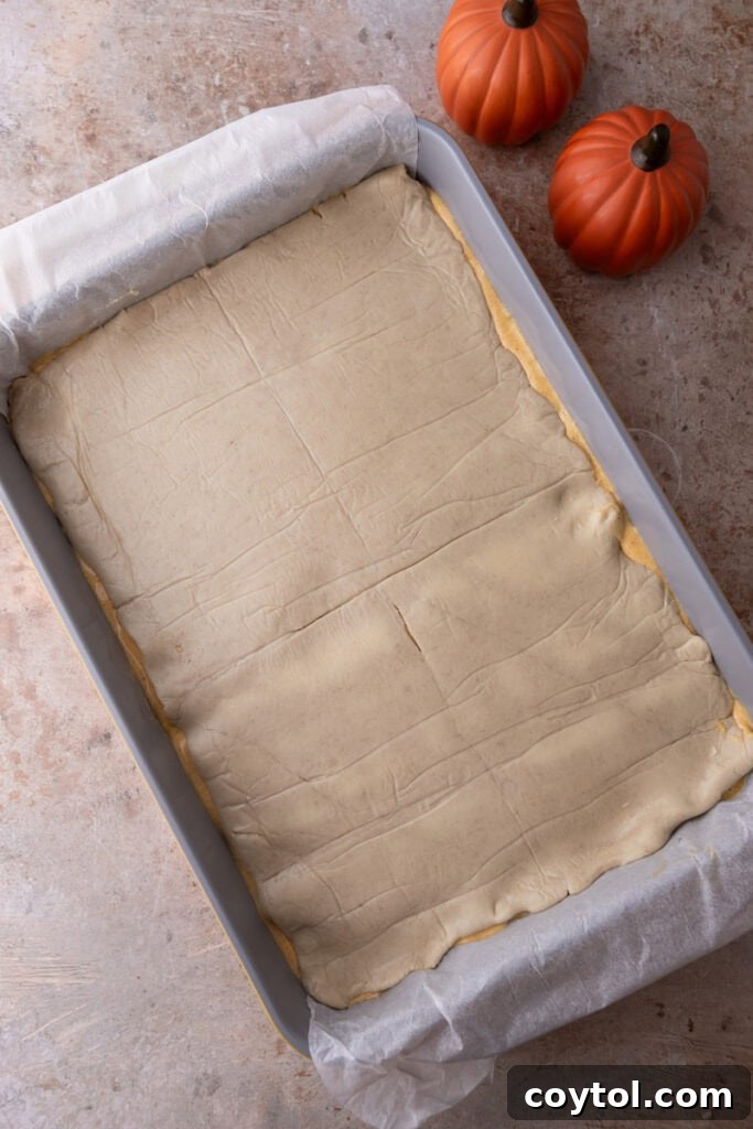 The second layer of croissant dough being carefully placed over the pumpkin cheesecake filling.