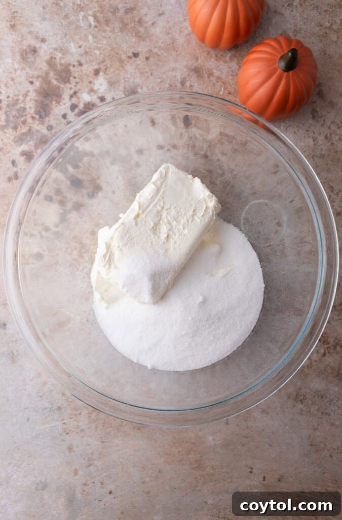 Cream cheese and sugar being beaten together in a mixing bowl until creamy.