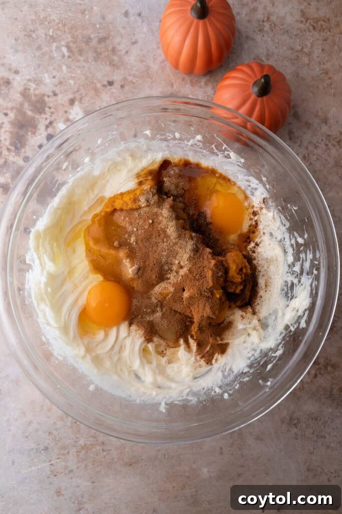 Eggs being added one by one to the cream cheese mixture, blending seamlessly.