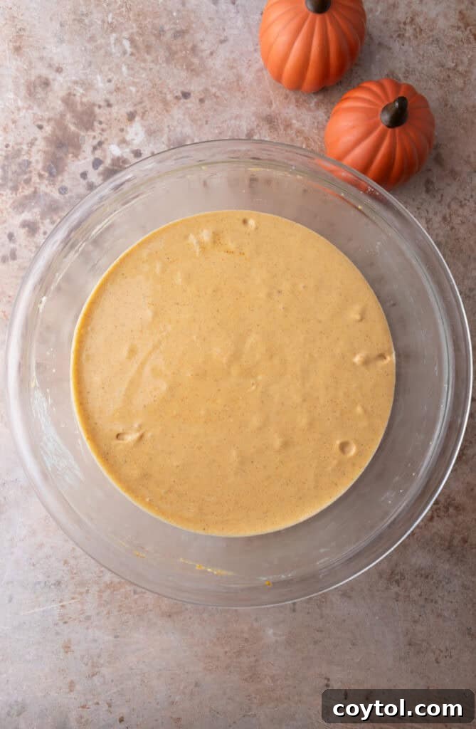 Pumpkin puree, vanilla, and spices stirred into the cheesecake mixture, creating a rich orange batter.