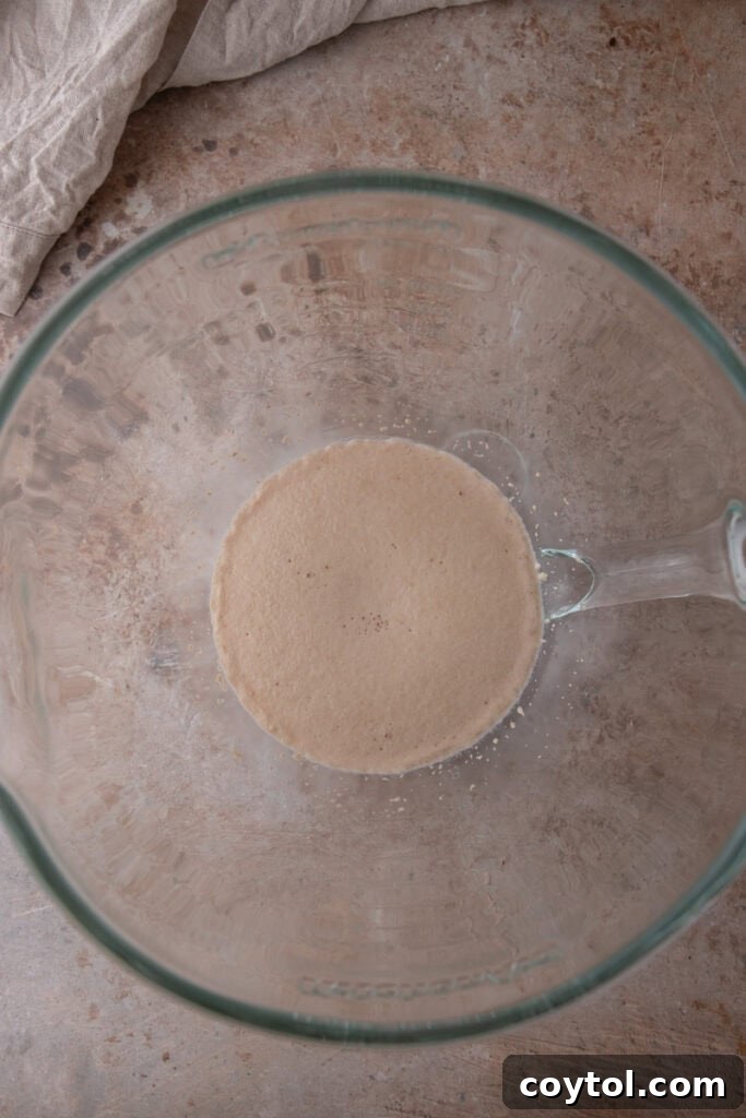 Pillowy Soft Buttery Holiday Rolls 5 Bloomed yeast and milk mixture in a large mixing bowl, showcasing a thick, foamy surface indicating active yeast