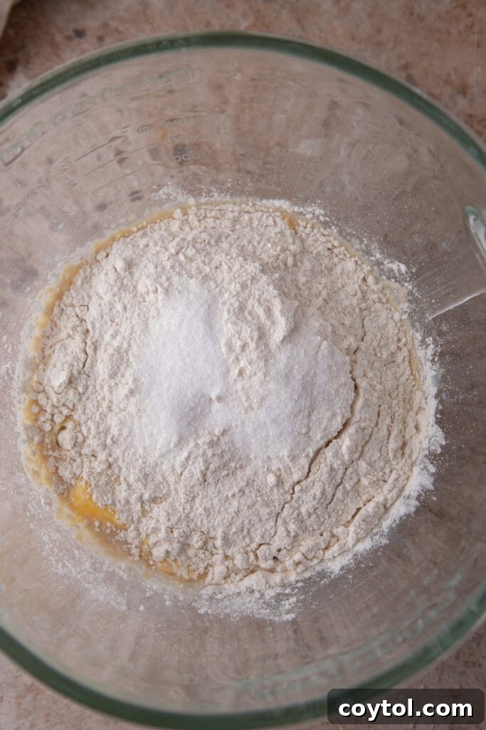 Pillowy Soft Buttery Holiday Rolls 7 Dry ingredients, including flour and salt, being added to the wet mixture in a stand mixer bowl