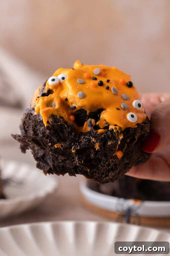 Hand holding frosted black cocoa cinnamon rolls