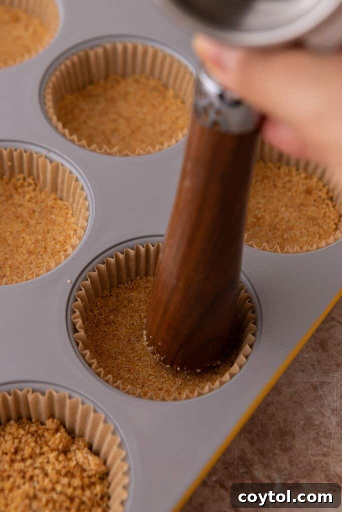 Irresistible Pecan Pie Cheesecake Bites 11 Muffin tin filled with unbaked graham cracker crusts, ready for baking.