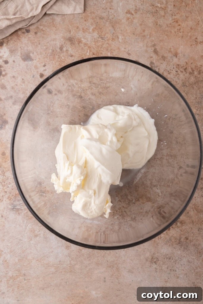 Irresistible Pecan Pie Cheesecake Bites 13 Cream cheese and sour cream being beaten together in a large mixing bowl for the cheesecake filling.