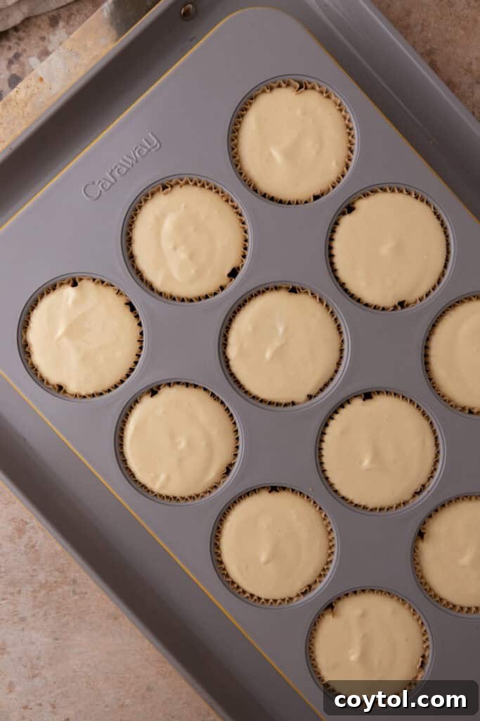 Irresistible Pecan Pie Cheesecake Bites 18 Cheesecake filling poured into muffin liners with crusts, ready for the water bath.