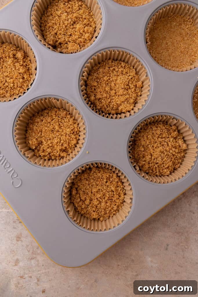 Irresistible Pecan Pie Cheesecake Bites 10 Graham cracker crust mixture being pressed into muffin liners.