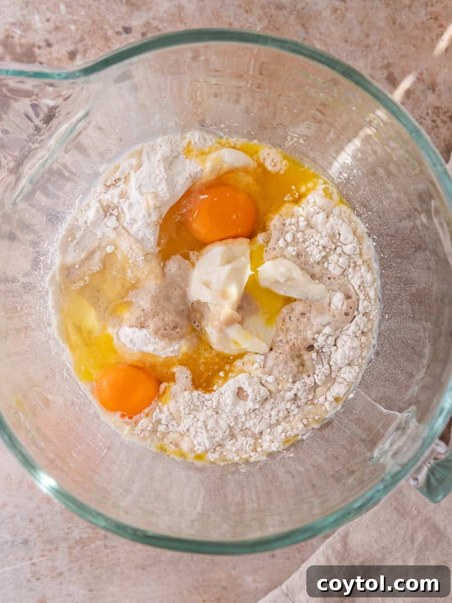 Cinnamon roll dough ingredients in mixing bowl with yeast, flour, butter, and eggs