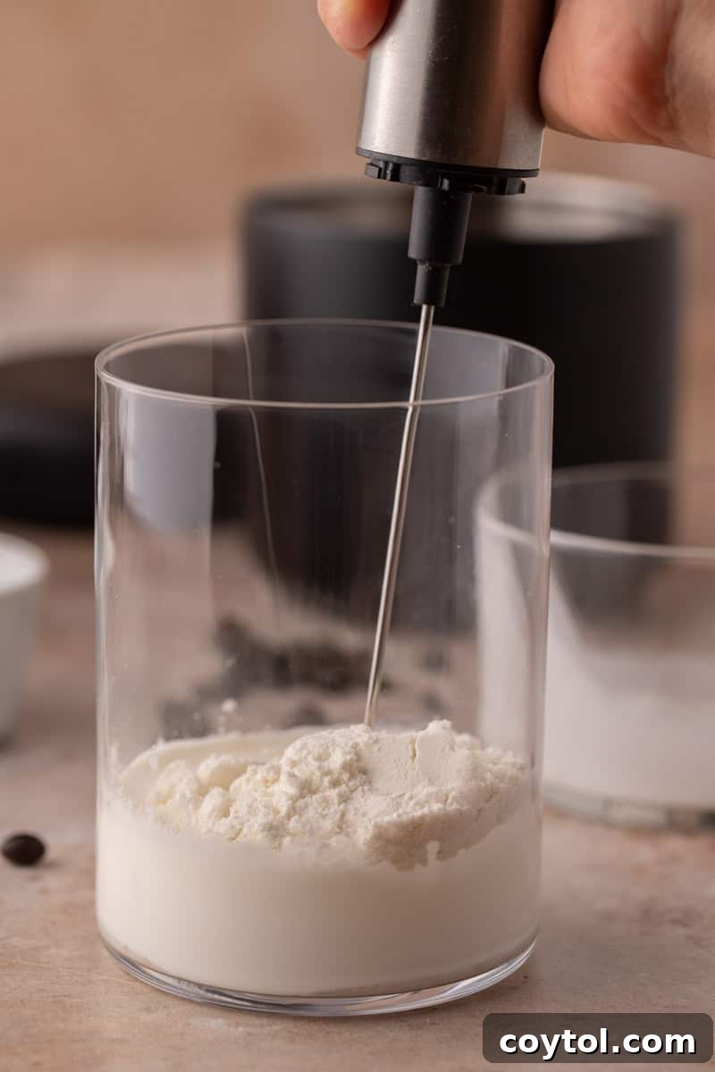 Handheld frother mixing cream and protein powder.