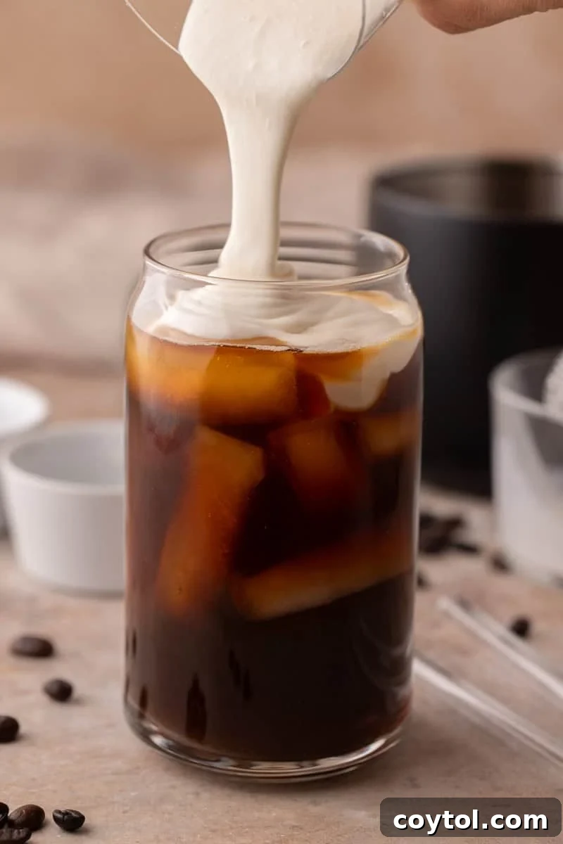 Thick homemade protein cold foam being poured over iced coffee.