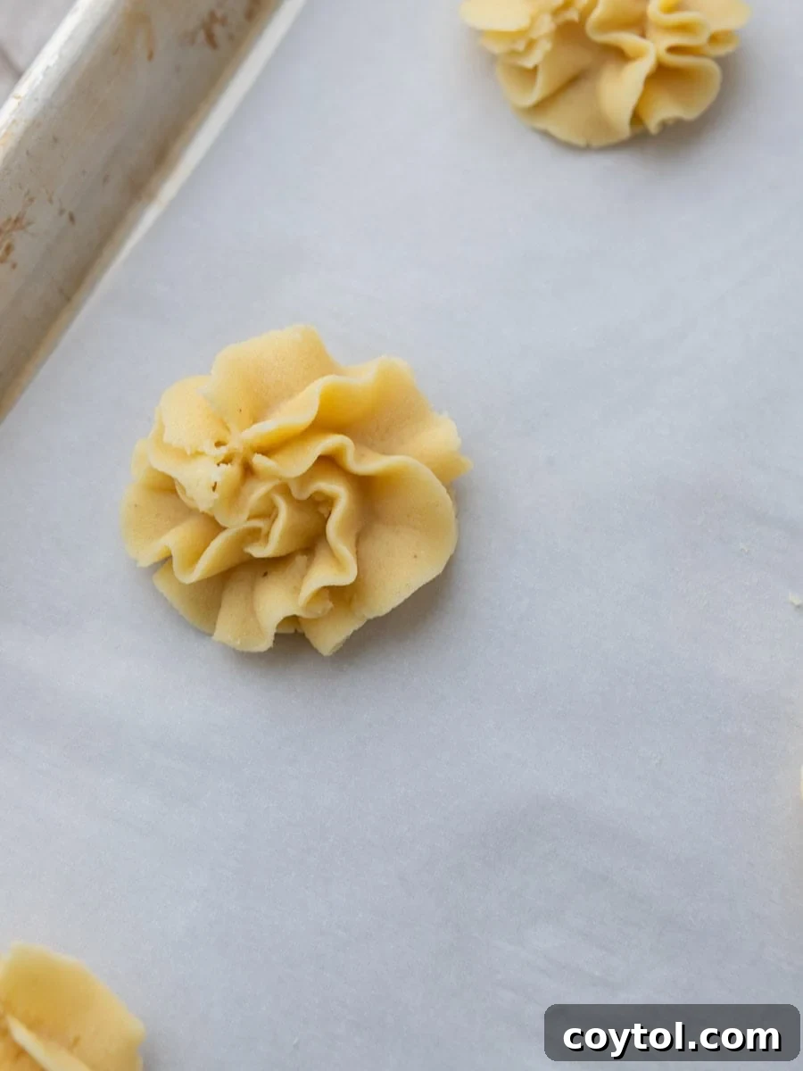 An unbaked piped butter cookie rosette, perfectly shaped and ready for chilling on a parchment-lined baking sheet.