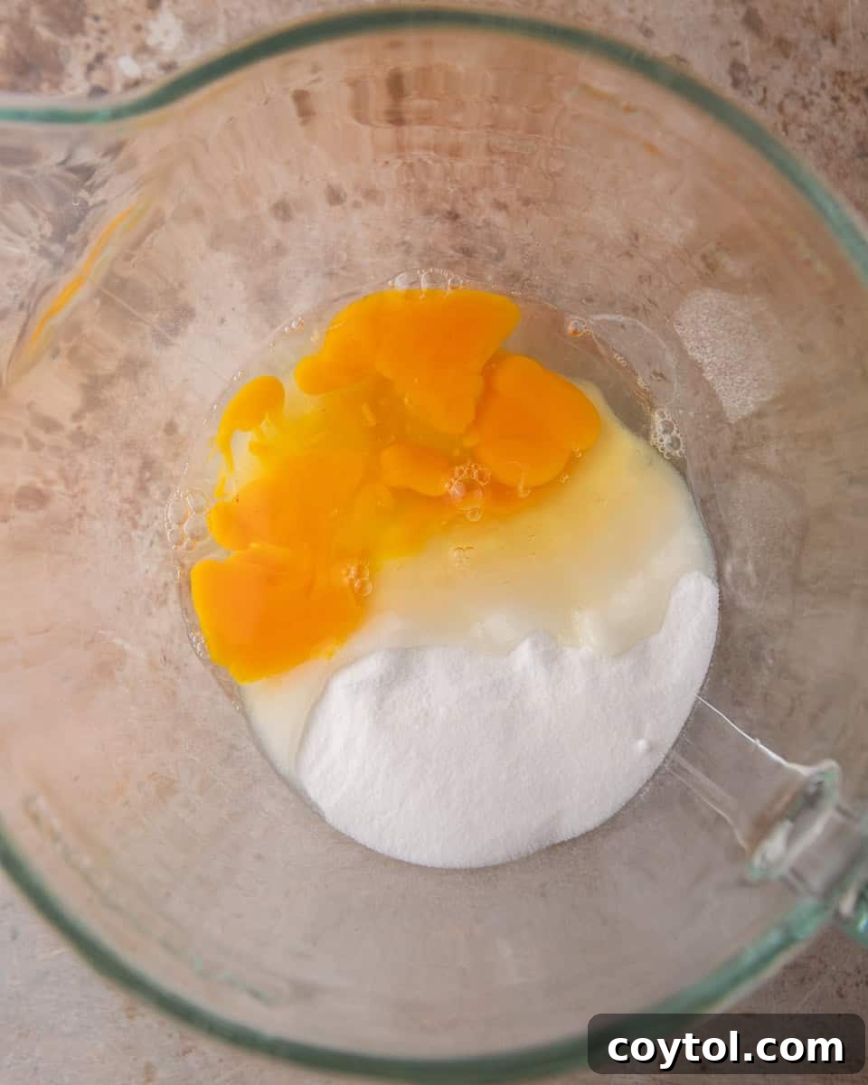 Large eggs and granulated sugar combined in a mixing bowl before whipping.