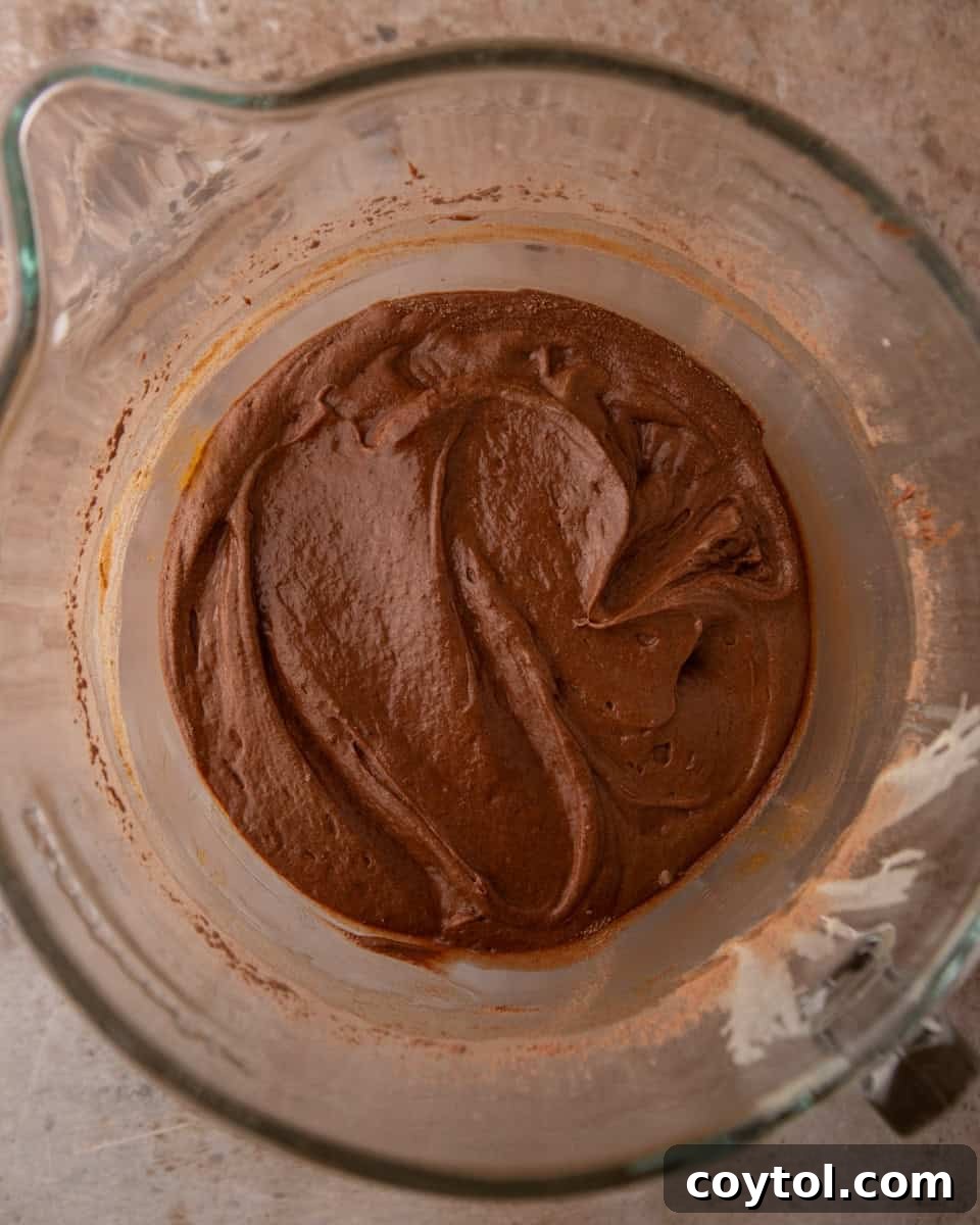 Thick, glossy chocolate brownie pudding batter stirred until perfectly smooth in a glass mixing bowl.