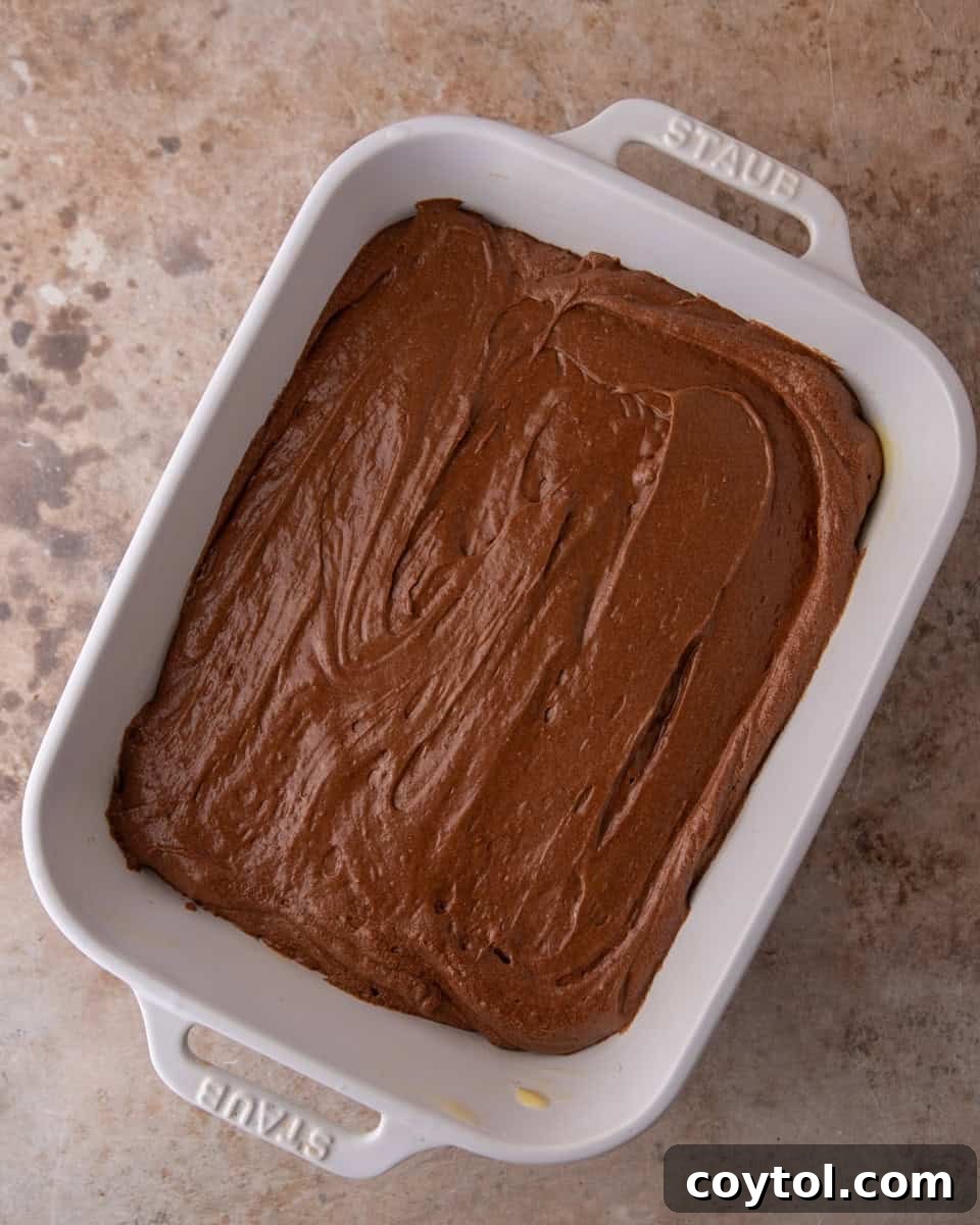 Brownie pudding batter evenly spread in a prepared baking dish, ready for the oven and water bath.
