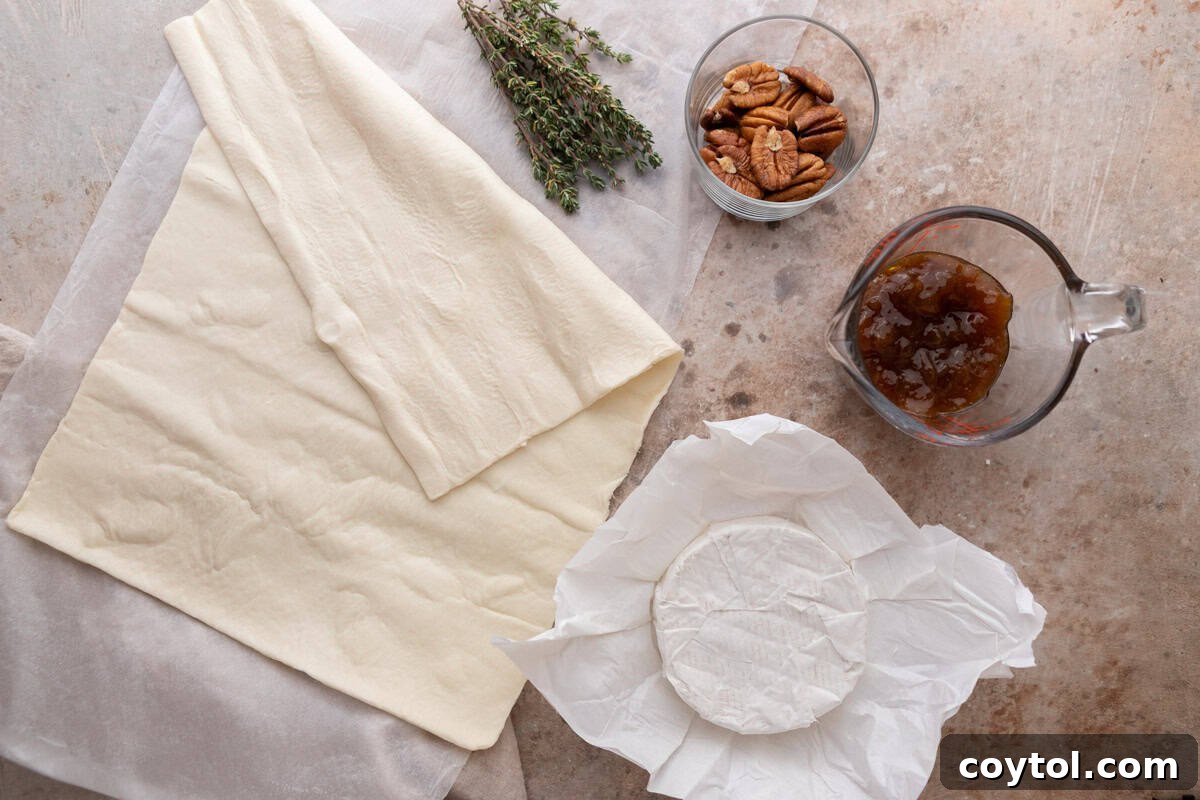 Sweet and Savory Brie Fig Pastry Bites 3 All the simple ingredients for brie and fig jam puff pastry cups neatly laid out on a kitchen counter: puff pastry, a wheel of brie cheese, a jar of fig jam, and a bowl of toasted pecans.