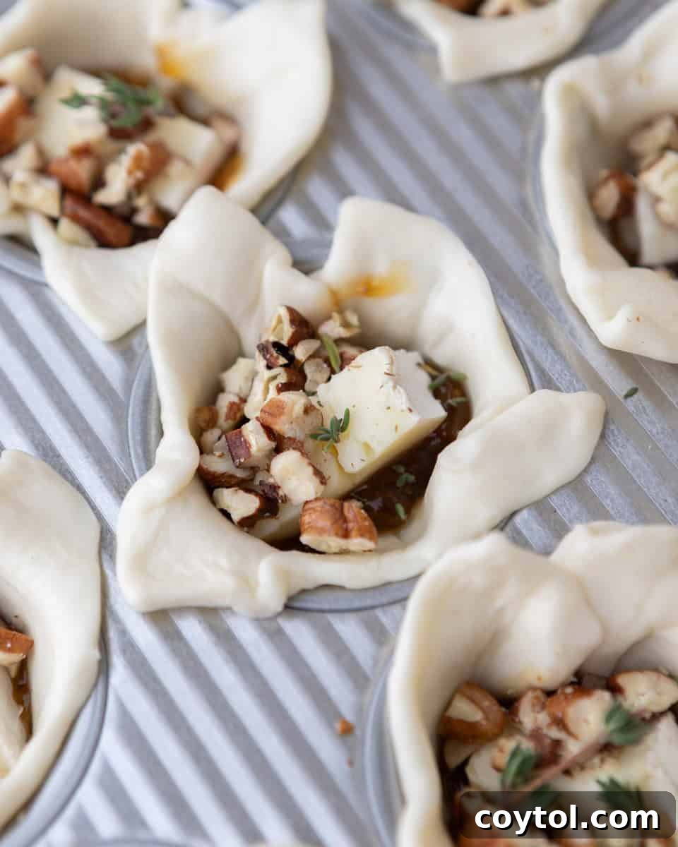 Sweet and Savory Brie Fig Pastry Bites 5 Unbaked puff pastry cups in a mini muffin tin, each filled with a piece of brie cheese, a spoonful of fig jam, and a sprinkle of toasted pecans.
