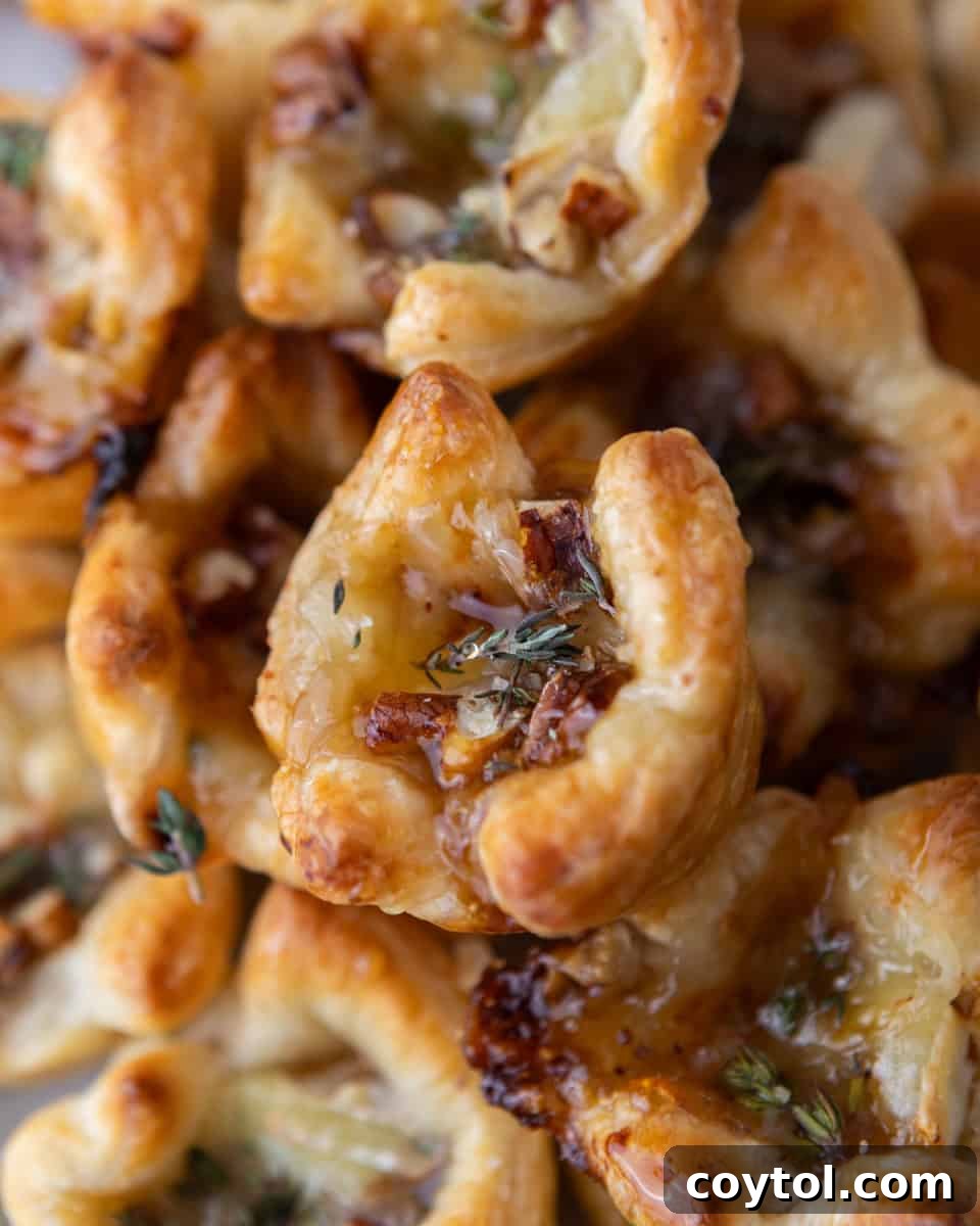 Sweet and Savory Brie Fig Pastry Bites 8 A close-up of a perfectly golden, flaky brie and fig jam puff pastry cup on a serving tray, adorned with a delicate rosemary sprig, ready for a festive gathering.