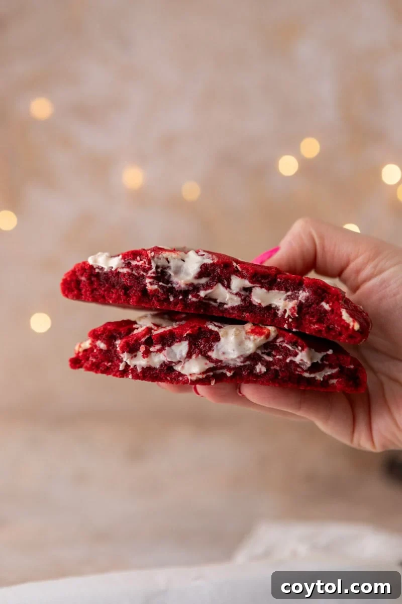 A single-serve red velvet cookie meticulously broken in half, showcasing its incredibly soft, thick, and chewy interior generously filled with melted white chocolate pieces.