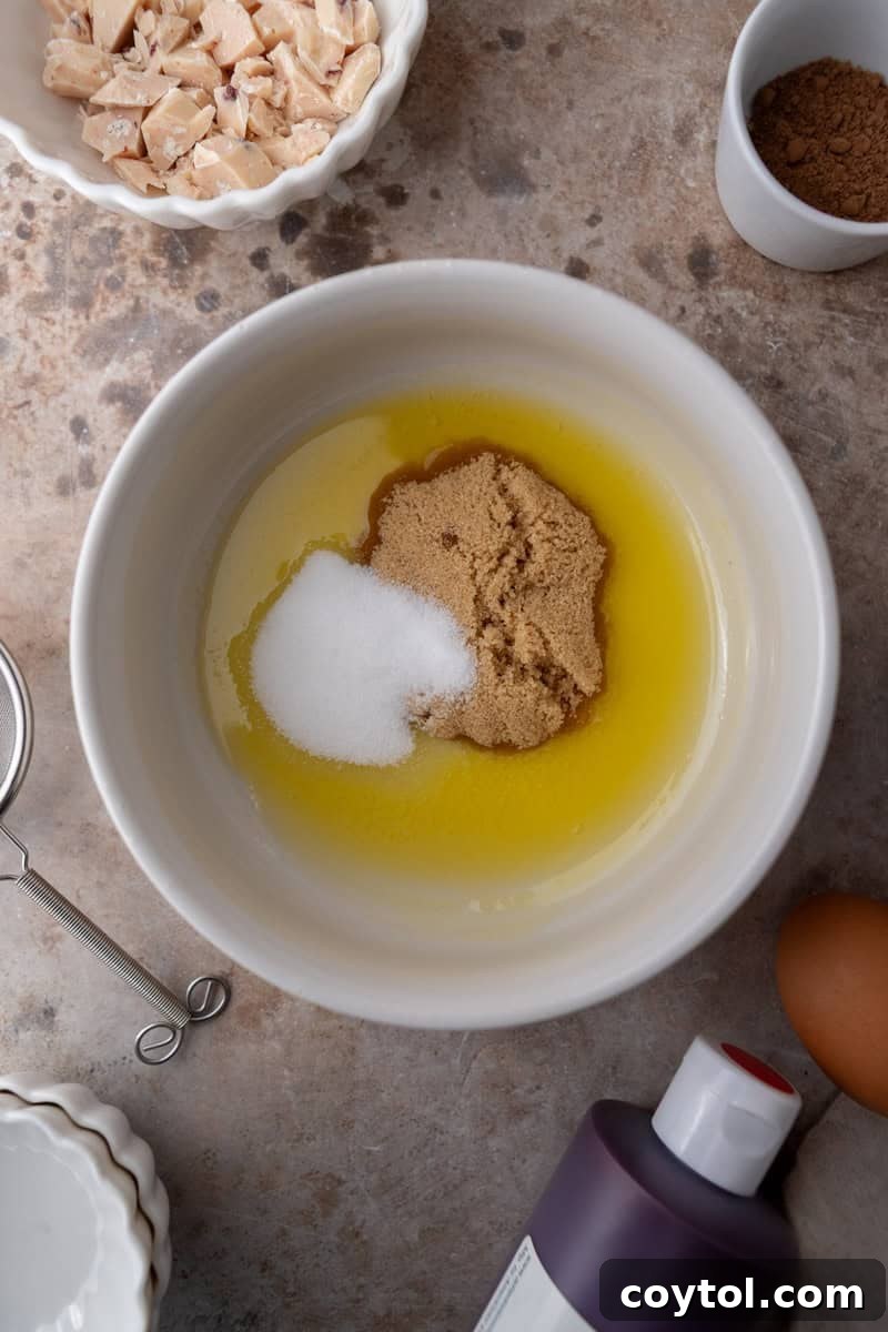 Melted butter mixed with brown sugar and white sugar in a bowl, creating a glossy, smooth base for the cookie dough.