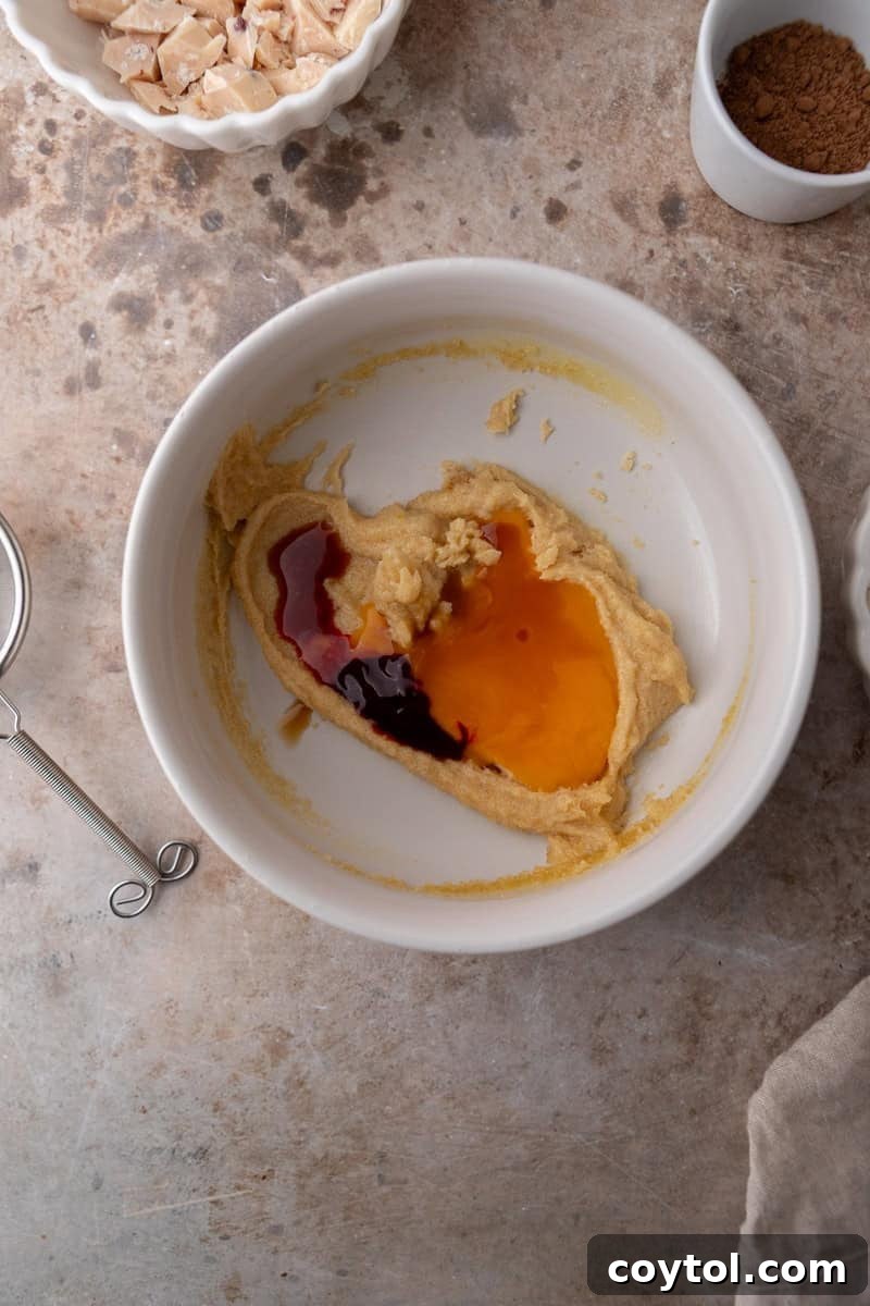 The vibrant red cookie dough mixture after the egg yolk, vanilla extract, and red food coloring have been whisked in, showing a smooth and shiny consistency.