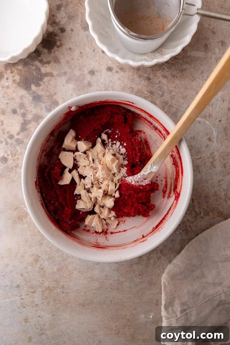 White chocolate chunks expertly folded into the vibrant red velvet cookie dough, ready for baking.