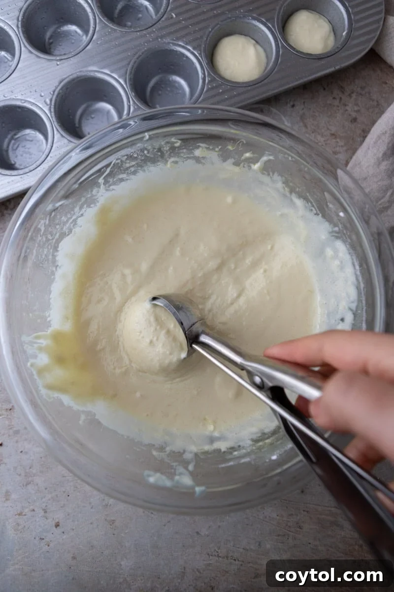 Scooping Brazilian cheese bread batter into mini muffin pan