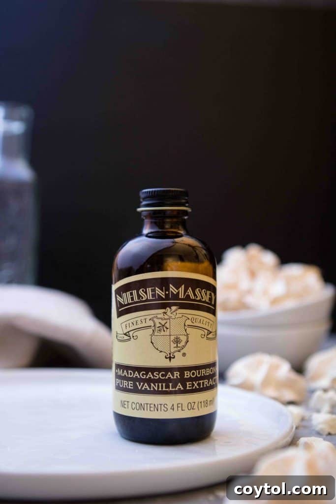 Nielsen Massey bourbon vanilla extract bottle next to freshly baked meringue cookies, highlighting a key ingredient.