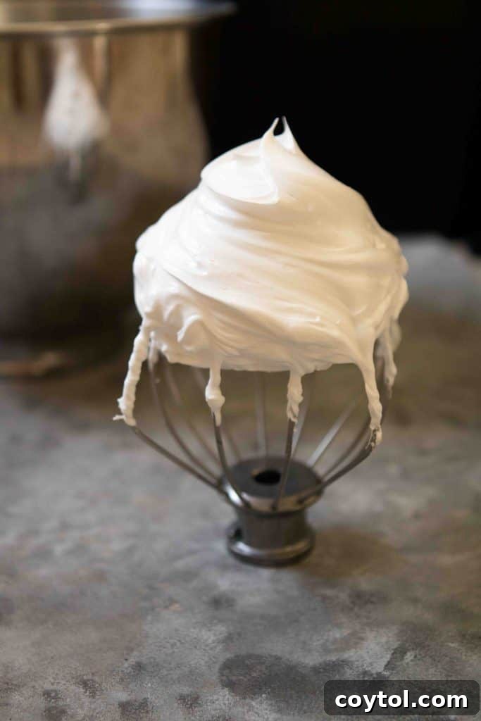 Detailed shot of perfectly whipped egg whites forming stiff peaks in a glass mixing bowl.