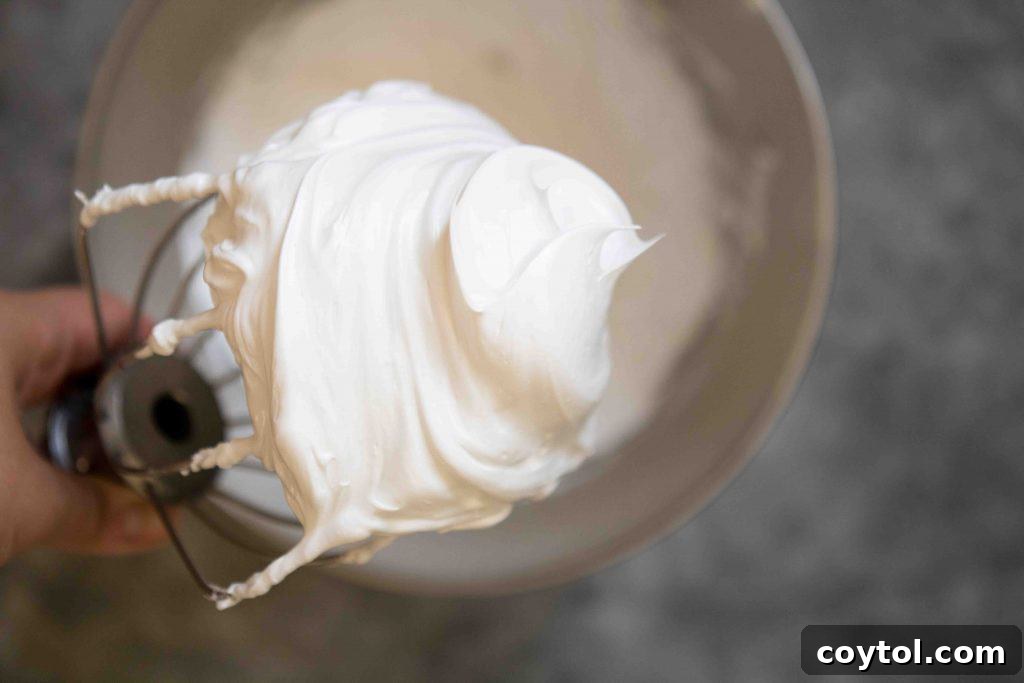 Close-up of perfectly whipped egg whites forming stiff, glossy peaks in a mixing bowl.