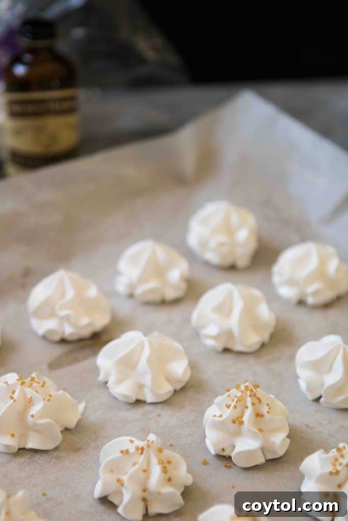 Meringue being piped onto a parchment-lined baking sheet using a star tip.