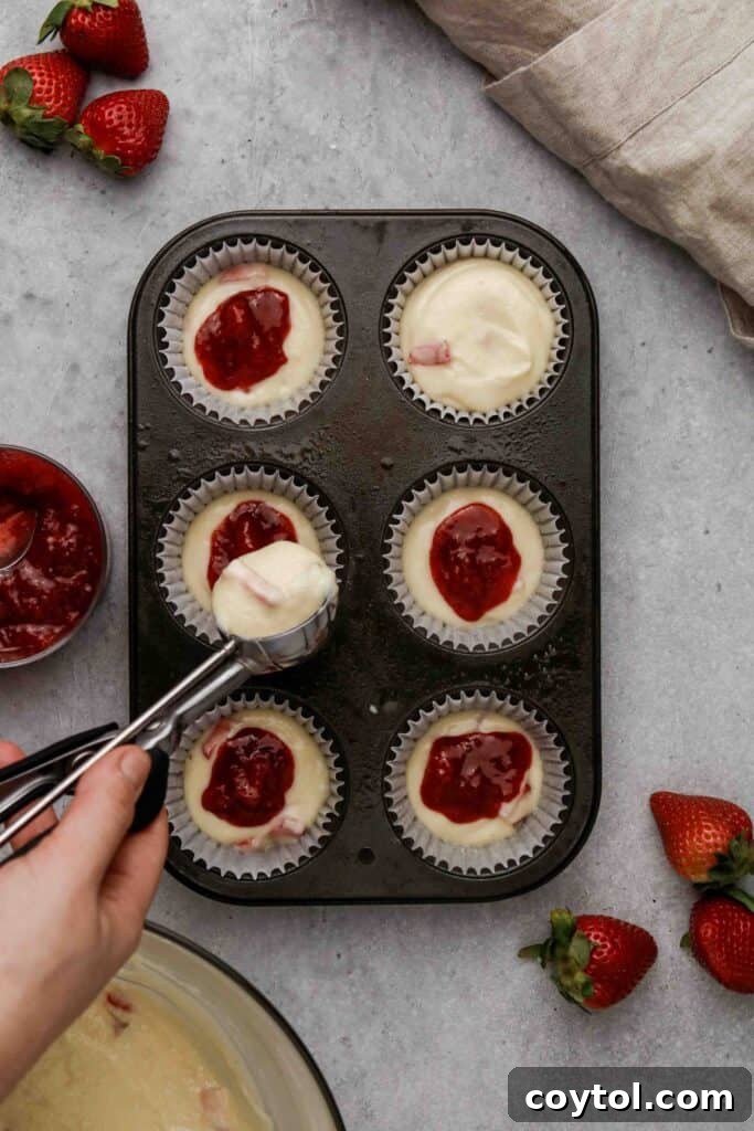 More muffin batter covering the strawberry jam, creating a surprise filling for the muffins.