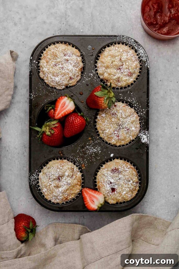 Freshly baked strawberry jam filled muffins, golden brown with a crunchy streusel topping, cooling in the pan.