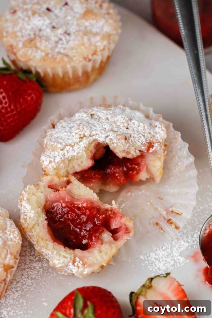 A close-up of a strawberry muffin with streusel, showing the gooey jam oozing out from its center, highlighting its delicious filling.