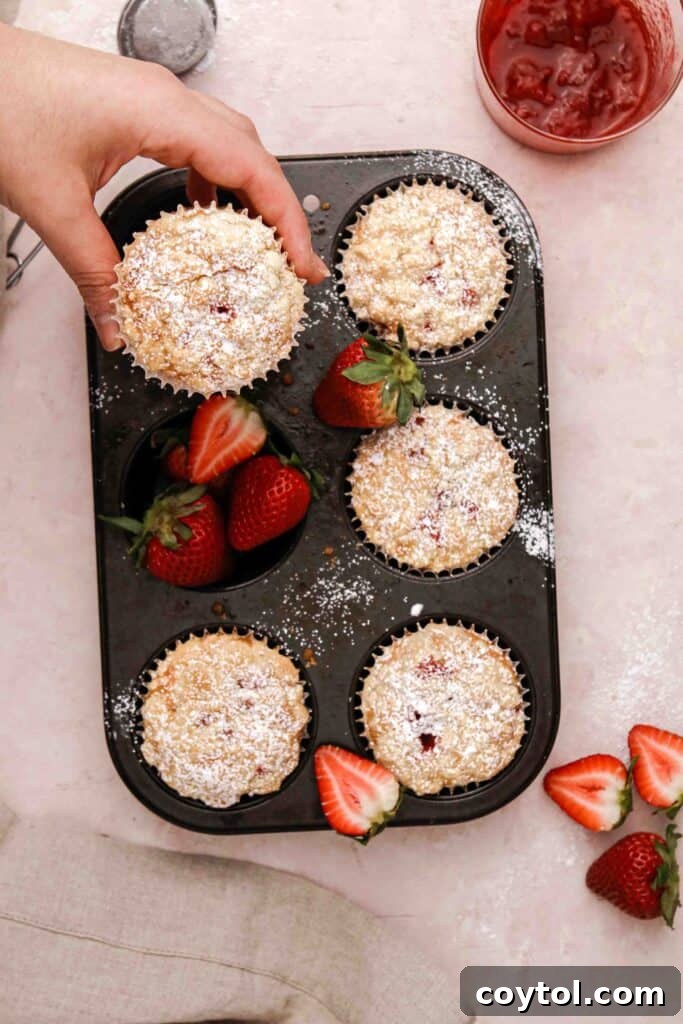 A hand reaching for a perfectly baked streusel strawberry muffin, showcasing its golden topping and inviting texture.