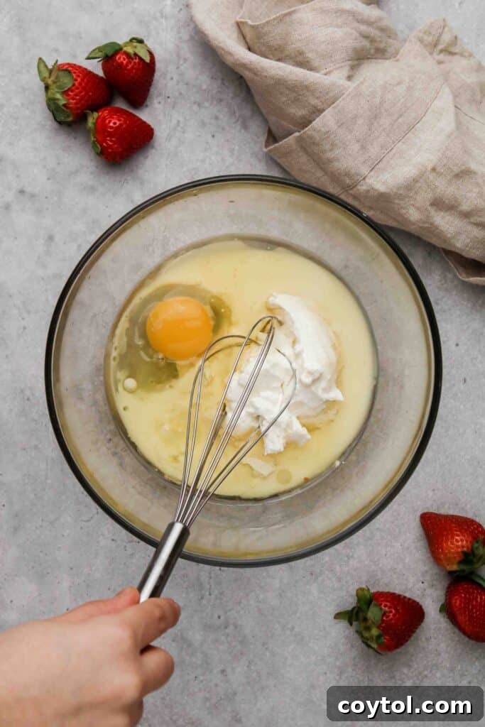 Wet ingredients, including Greek yogurt and egg, being whisked together in a medium bowl.